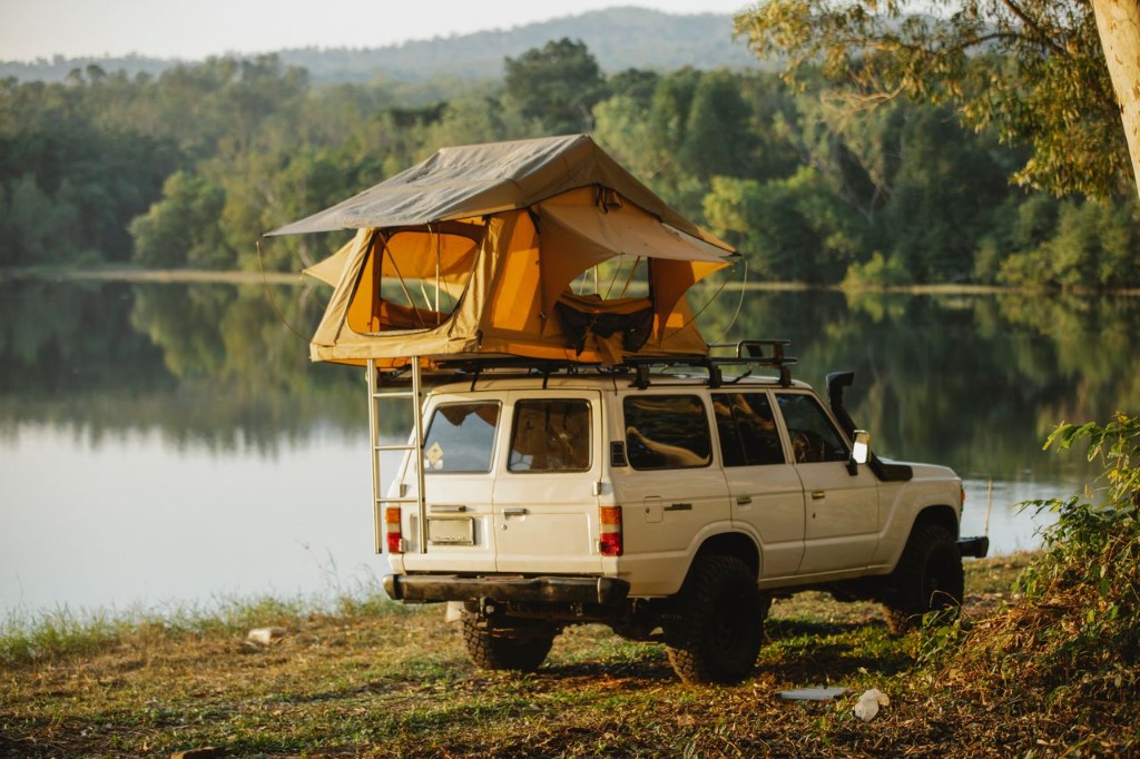Land Cruiser with rooftop tent deployed beside a calm lake at golden hour